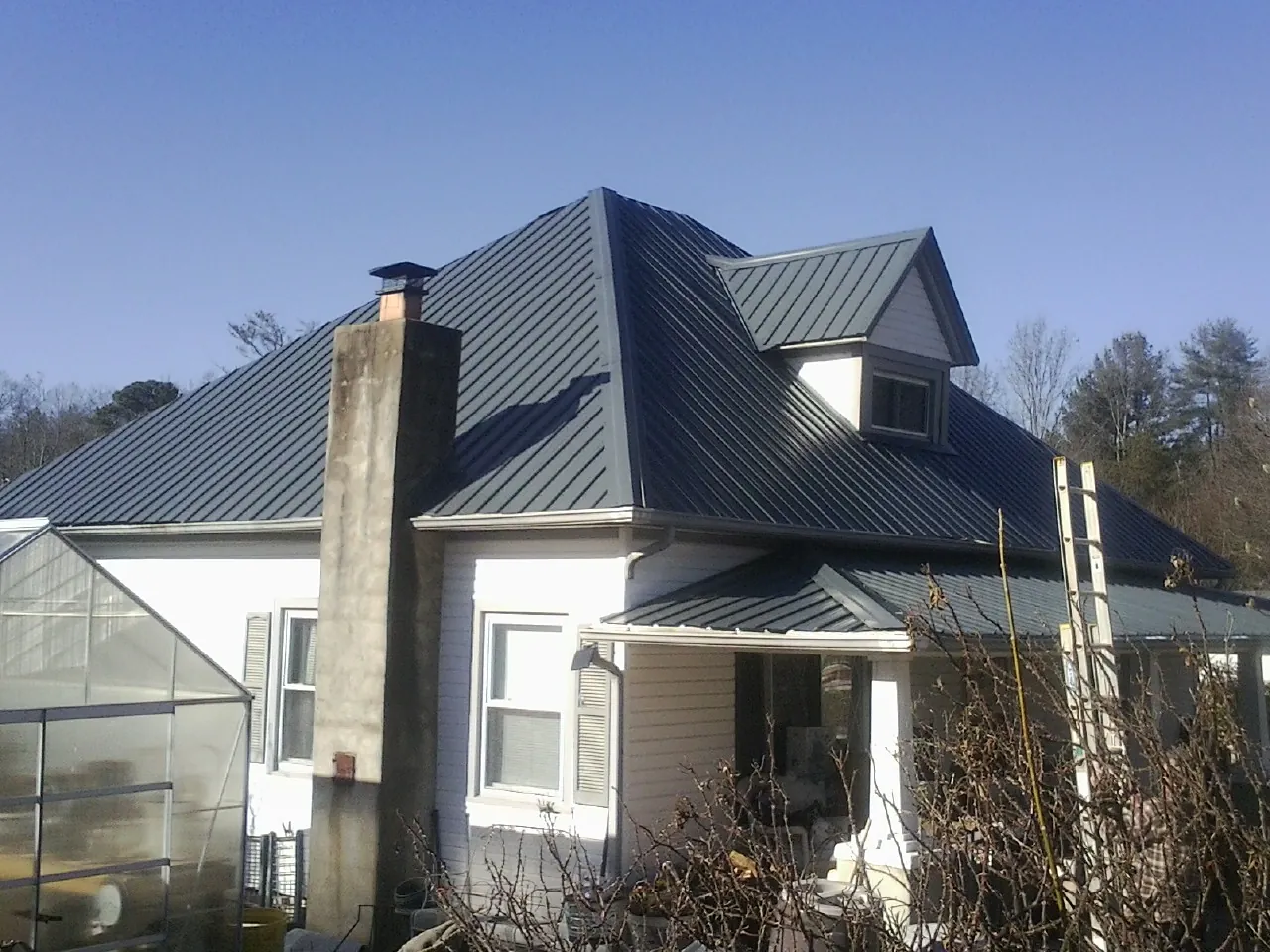 Dark blue standing seam metal roof on a white farmhouse with dormer — Slate & Tile Roof Repair by Roofing Brothers in Flinton