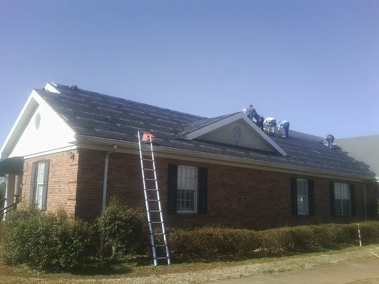 Crew tearing shingles off a brick ranch roof with a ladder set — Emergency Roof Repair work by our crew in Flinton