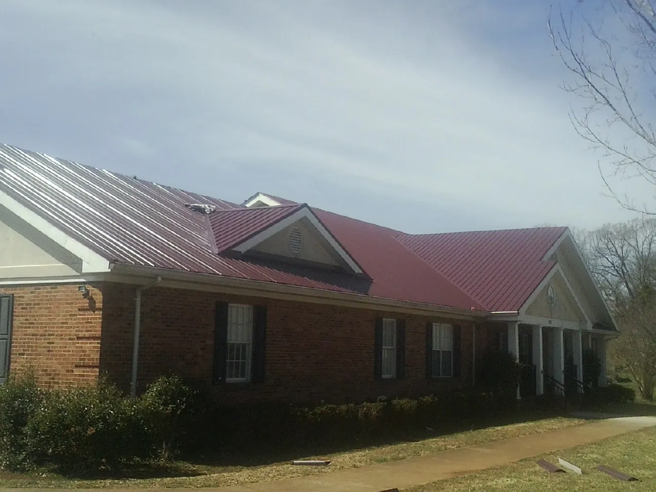 Red metal roof with gabled entries on a long brick building, from a Hail Damage Roof Repair job in Flinton