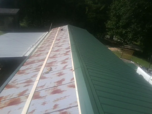 Old rusted panels beside newly installed green metal roofing — Wind Damage Roof Repair by Roofing Brothers in Flinton