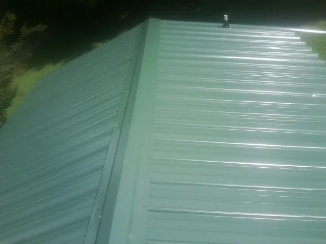 New green metal panels meeting at the ridge of a roof — Flat Roof Repair work by our crew in Flinton