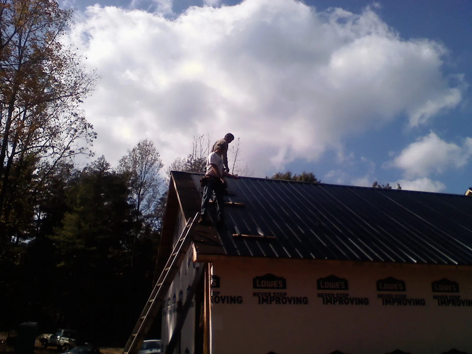 Roofer fastening dark metal panels high against a cloudy sky in Flinton
