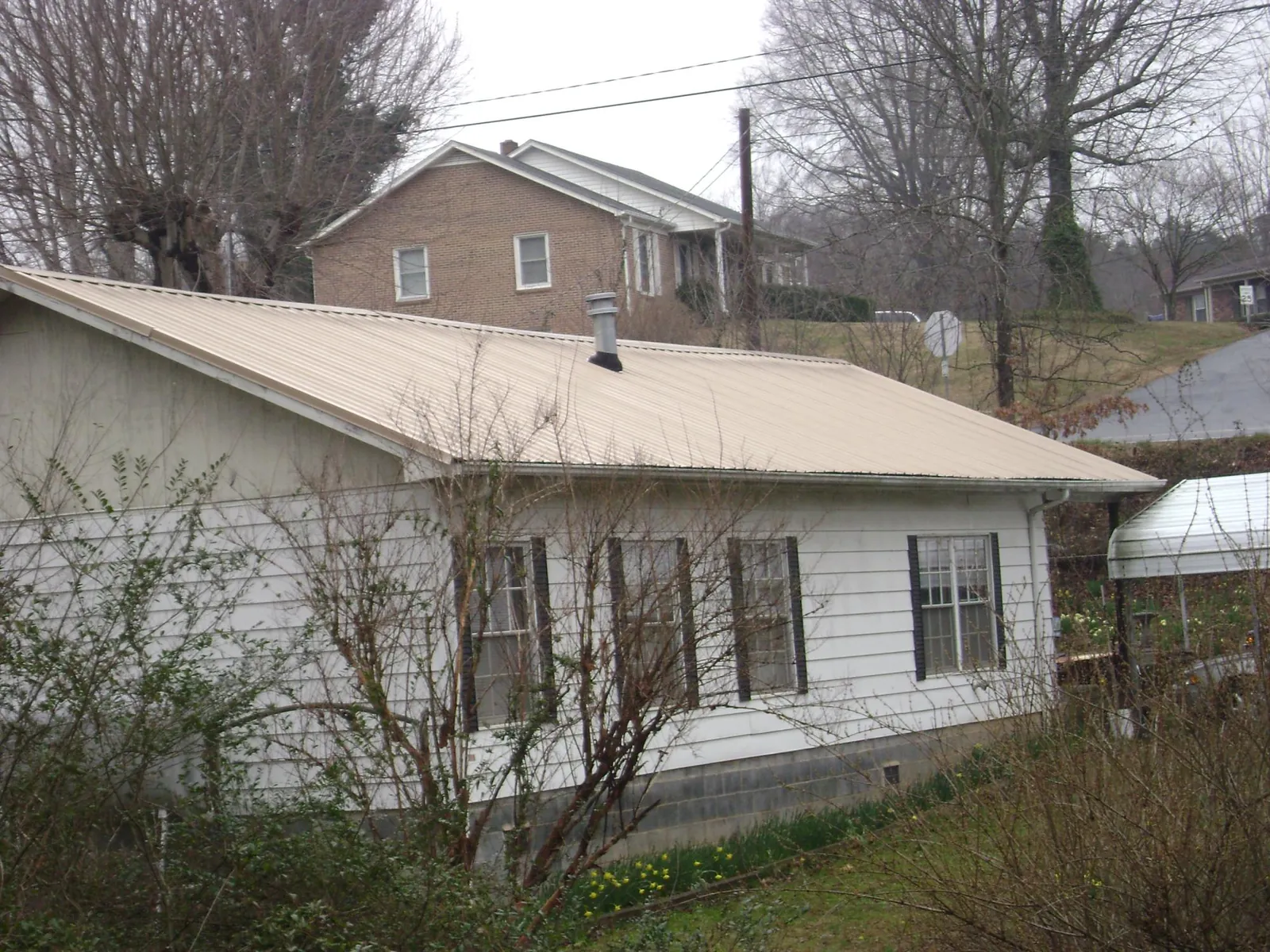 Tan metal roof on a white sided house set into a hillside — Commercial Roofing by Roofing Brothers in Flinton
