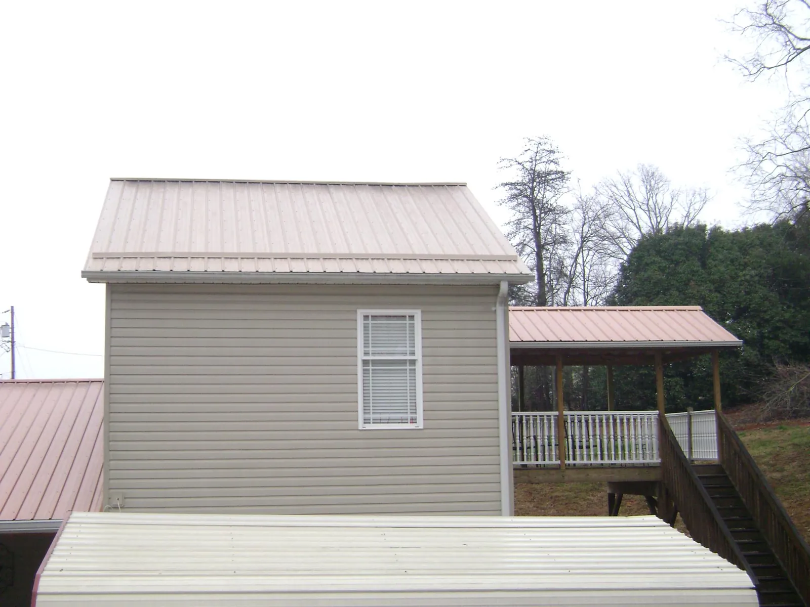 Tan metal roofs on a two story addition and attached porch, from a Roof Replacement job in Flinton